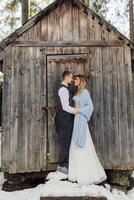 jeune marié et la mariée sur le Contexte de une en bois forêt maison. le la mariée est enveloppé dans une bleu couverture. hiver mariage. photo