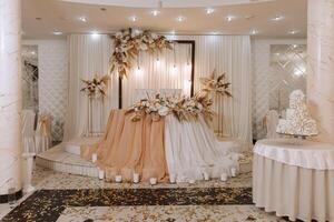 le mariage table de le la mariée et marié, décoré avec fleurs, séché oreilles de blé et blanc tulle, est fabriqué dans nu couleur. fleurs sur des stands. mariage détails. lumière photo