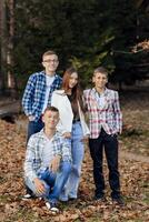quatre adolescents de différent les sexes, posant dans la nature. adolescent camarades de classe sont repos contre le Contexte de un l'automne forêt. photo