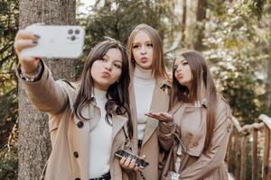 Trois Jeune femmes prise selfie avec intelligent mobile téléphone en plein air - content magnifique femelle copains souriant à caméra en plein air - mode de vie concept avec de bonne humeur les filles profiter Extérieur vacances. photo