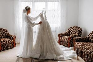 une la mariée dans une soie costume et voile pose dans sa pièce suivant à sa mariage robe. Matin de le la mariée. préparation. mariage la photographie photo