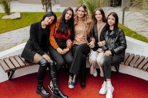 groupe de souriant et content adolescent copains portant décontractée vêtements dépenses temps ensemble, posant et parlant avec chaque autre près Université bâtiment sur l'automne journée. photo