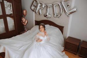 une luxueux la mariée avec une magnifique coiffure et une magnifique robe est avoir prêt pour le mariage la cérémonie dans le Matin. Matin photo de le la mariée à Accueil ou dans une Hôtel chambre. professionnel se maquiller.