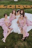 groupe portrait de le la mariée et demoiselles d'honneur. la mariée dans une mariage robe et demoiselles d'honneur dans rose ou poudre Robes et en portant élégant bouquets sur le mariage journée. photo