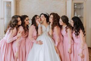 portrait de le la mariée avec sa copains dans le chambre. une brunette la mariée dans une longue blanc robe et sa copains dans rose Robes sont souriant et heureux. Jeune filles. photo