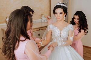 une ami aide le la mariée boucler sa robe. une femme aide sa ami boucler le boutons sur le retour de sa mariage robe. le Matin de le mariée, le création de une famille, un important événement. photo