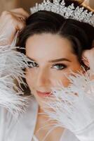 Matin de le la mariée avant le mariage. une magnifique Jeune femme avec une voile et une magnifique coiffure dans une blanc peignoir dans une pièce avec une magnifique intérieur. Naturel beauté et professionnel se maquiller. photo