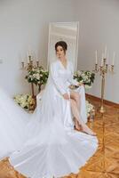 une magnifique brunette la mariée est avoir prêt pour le mariage dans une magnifique boudoir style tenue séance sur une chaise parmi Frais fleurs et élégant chandeliers. mariage portrait, photo. photo