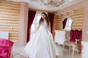 une magnifique magnifique portrait de une Jeune la mariée. magnifique la mariée avec mariage maquillage et bijoux couronne sur longue frisé cheveux. mariage photo modèle avec marron yeux dans une magnifique intérieur.