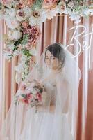 une brunette la mariée dans une tiare pose avec une bouquet de blanc et rose fleurs. magnifique cheveux et se maquiller. printemps mariage photo