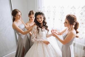 copains réjouir avec le la mariée dans le Matin. elles ou ils prendre des photos, sourire, Aidez-moi le la mariée boucler sa robe. photo