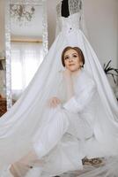 une content la mariée est en train de préparer pour sa luxueux mariage dans une Hôtel chambre, avec une mariage robe sur une mannequin proche. portrait de une femme avec à la mode cheveux, maquillage et une sourire dans une pansement robe. photo