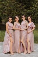 groupe portrait de le la mariée et demoiselles d'honneur. la mariée dans une mariage robe et demoiselles d'honneur dans rose ou poudre Robes et en portant élégant bouquets sur le mariage journée. photo