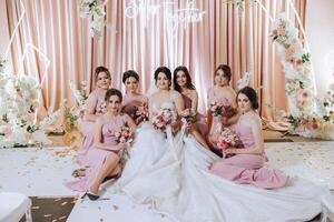 groupe portrait de le la mariée et demoiselles d'honneur. la mariée dans une mariage robe et demoiselles d'honneur dans rose ou poudre Robes et en portant élégant bouquets sur le mariage journée. photo