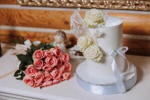 une grand luxueux à plusieurs niveaux mariage gâteau est décoré avec Frais blanc Rose fleurs dans le banquet salle. mariage dessert en dessous de le soir lumière. mariage décor. photo