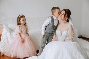 le la mariée est photographié avec petit les enfants sur le mariage journée. une peu garçon baisers le sien la mariée sur le joue. photo