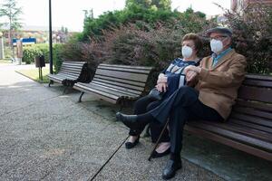 Sénior couple avec masques séance dans une ville banc photo