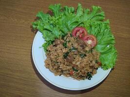 délicieux indonésien frit riz nasi goreng avec beaucoup de laitue, moutarde légumes verts et tomates servi sur une blanc assiette photo