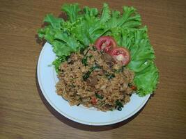 délicieux indonésien frit riz nasi goreng avec beaucoup de laitue, moutarde légumes verts et tomates servi sur une blanc assiette photo