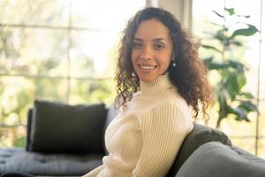 femme latine souriante et assise sur un canapé photo