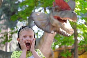 une enfant cris à le vue de une dinosaure. adolescent garçon dans dinoparc. photo
