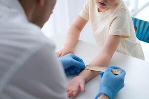 une Masculin médecin fait du un important mantoux tester sur une enfant. le médecin les mesures le mantoux tester avec une règle pour une peu garçon photo