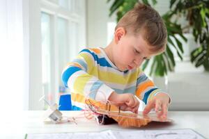 peu garçon performant ou en train d'étudier science avec fils, Connexions. électronique expérience. le enfant est expérimenter à maison. photo