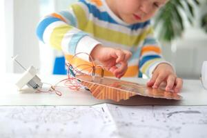 peu garçon performant ou en train d'étudier science avec fils, Connexions. électronique expérience. le enfant est expérimenter à maison. photo