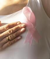 coup de le femme contre le blanc mur dans le blanc Haut avec rose ruban, comme une symbole de une Sein cancer conscience, performant soi examen de le seins, à la recherche pour anomalies. concept photo