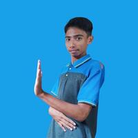 Jeune asiatique homme avec Arrêtez main. avec une sérieux visage portant une bleu T-shirt, isolé sur une bleu Contexte photo
