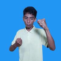 le enthousiaste visage de le asiatique jeunesse serré le sien les poings bleu Contexte. photo