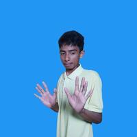 Jeune asiatique homme mains arrêt. avec une sérieux visage portant une Jaune T-shirt, isolé sur une bleu Contexte photo