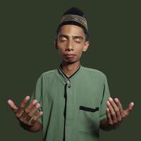 Jeune asiatique homme prier portant vert musulman vêtements pendant Ramadan vert Contexte photo