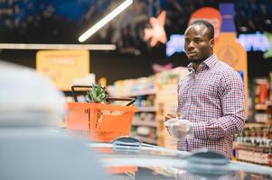 portrait de souriant homme à supermarché. Jeune africain homme avec achats panier dans épicerie boutique photo