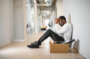 portrait coup de africain américain triste homme d'affaire dans costume et attacher séance avec boîte de truc. Masculin Bureau ouvrier perdu emploi. chômage taux croissance. mis à la porte dérangé désespéré homme photo