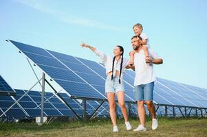 une large coup de une content famille permanent ensemble et souriant à caméra avec une grand solaire panneau dans Contexte photo