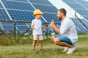 une père et le sien peu fils près le solaire panneaux. une peu garçon dans une Jaune casque photo