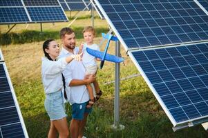 Jeune famille de Trois est accroupi près photovoltaïque solaire panneau, peu garçon et parents. moderne famille concept. le concept de vert énergie photo