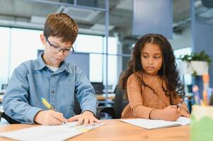 concentré multiracial élèves des gamins l'écriture vers le bas Les données dans carnet tandis que séance à table photo