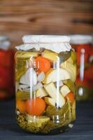 verre pots avec mariné concombres cornichons, mariné tomates et chou. pots de divers mariné des légumes. en conserve nourriture dans une rustique composition. photo