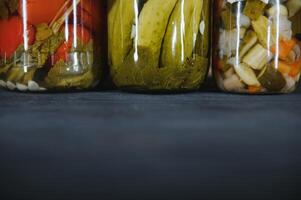 verre pots avec mariné concombres cornichons, mariné tomates et chou. pots de divers mariné des légumes. en conserve nourriture dans une rustique composition. photo