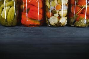 en conserve concombres et tomates avec artisanat couvercles sur une en bois Contexte. concombres et tomates avec endroit pour texte. les stocks de en conserve aliments. récolte, les stocks pour le l'hiver. photo