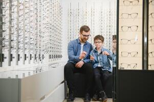 papa et fils choisir Nouveau élégant des lunettes dans un optique magasin. vision se soucier concept photo