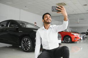 Beau Indien homme prise une selfie avec voiture clés à le sien Nouveau voiture à le concession salle d'exposition fond La technologie social médias partage positivité mode de vie en voyageant tourisme. photo