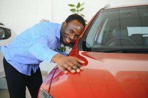 Nouveau voiture propriétaire. content africain américain homme émouvant étreindre le sien tout neuf auto photo