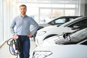 Jeune homme achat premier électrique voiture dans le salle d'exposition. éco voiture vente concept photo