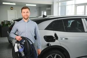 barbe homme en essayant une Nouveau mise en charge câble avec une voiture mise en charge station à le moteur concession. concept de achat électrique véhicule. intelligent écologique vivant photo