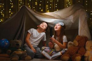 deux peu enfant jouer à Accueil dans le soir à construire une camping tente à lis livres avec une lampe de poche et sommeil à l'intérieur. concept de jeu, la magie, la créativité, alarme systèmes. photo