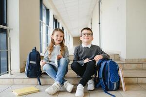 portrait de souriant école des gamins dans école couloir avec livres photo