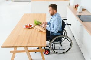 Jeune désactivée homme séance sur roue chaise en train de préparer nourriture dans cuisine photo